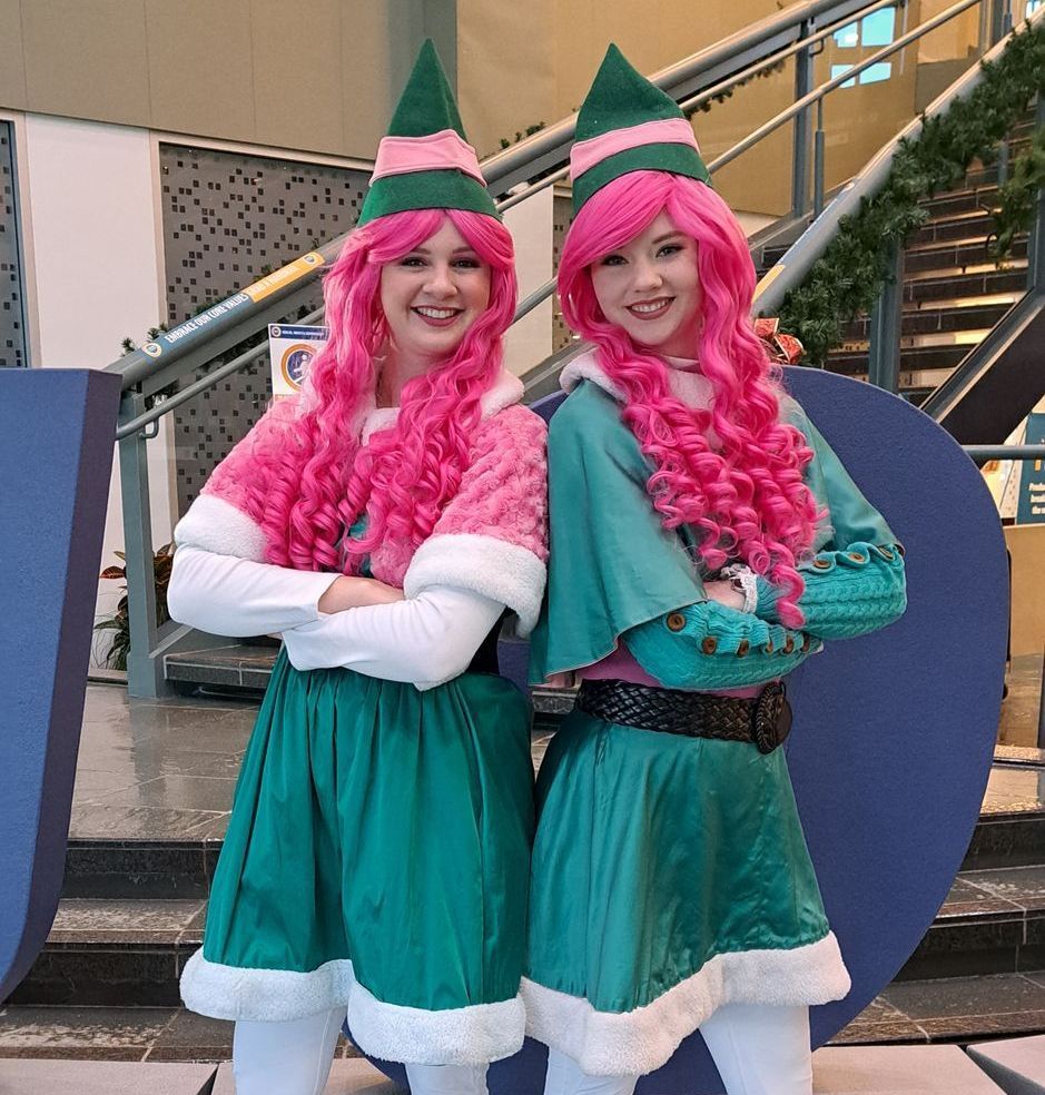Two girls dressed as elves with pink hair are posing for a picture at at corporate Christmas party in Calgary, Alberta