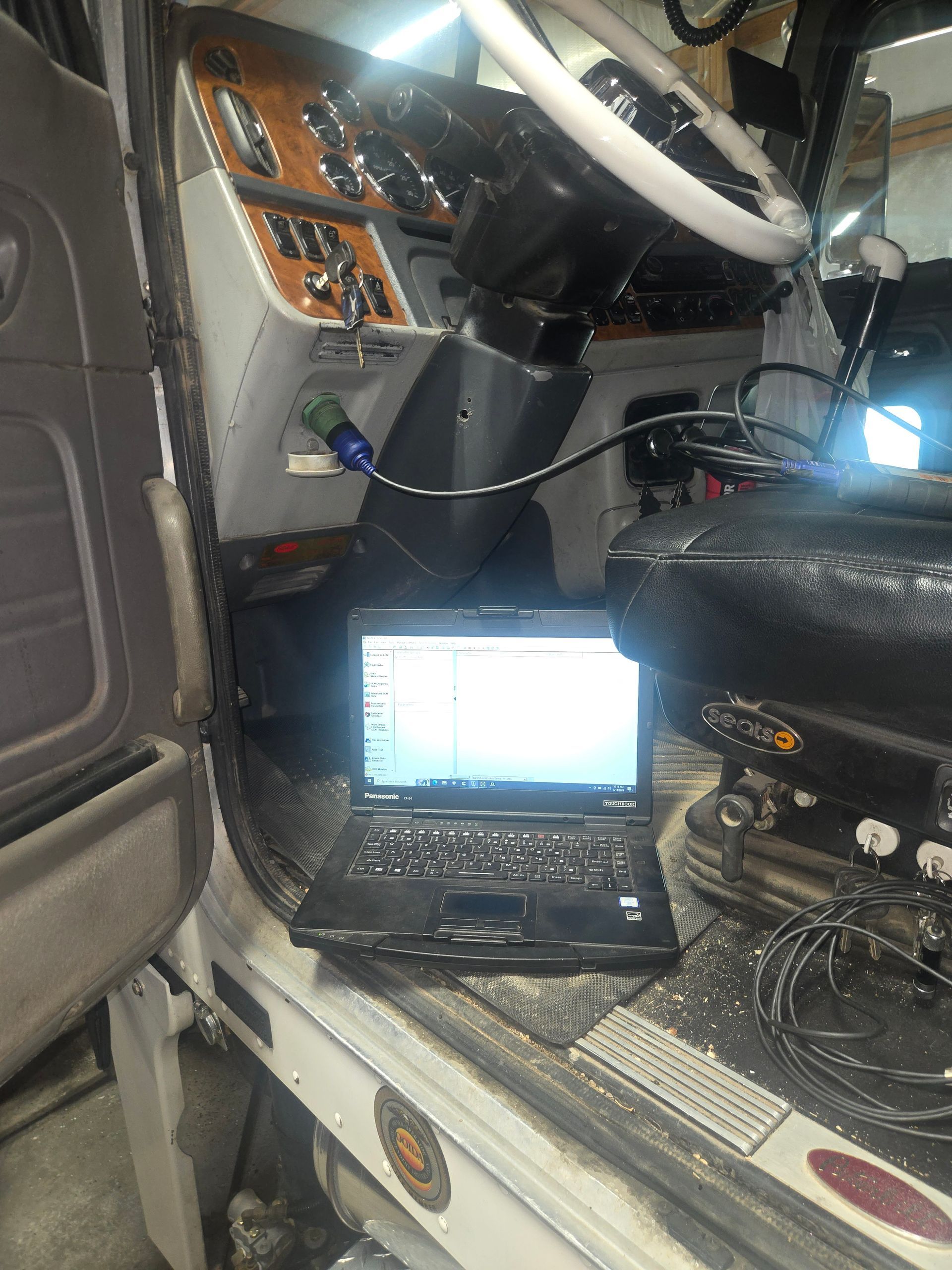 Mechanic using laptop under a vehicle, analyzing data. Workshop setting, focused expression.