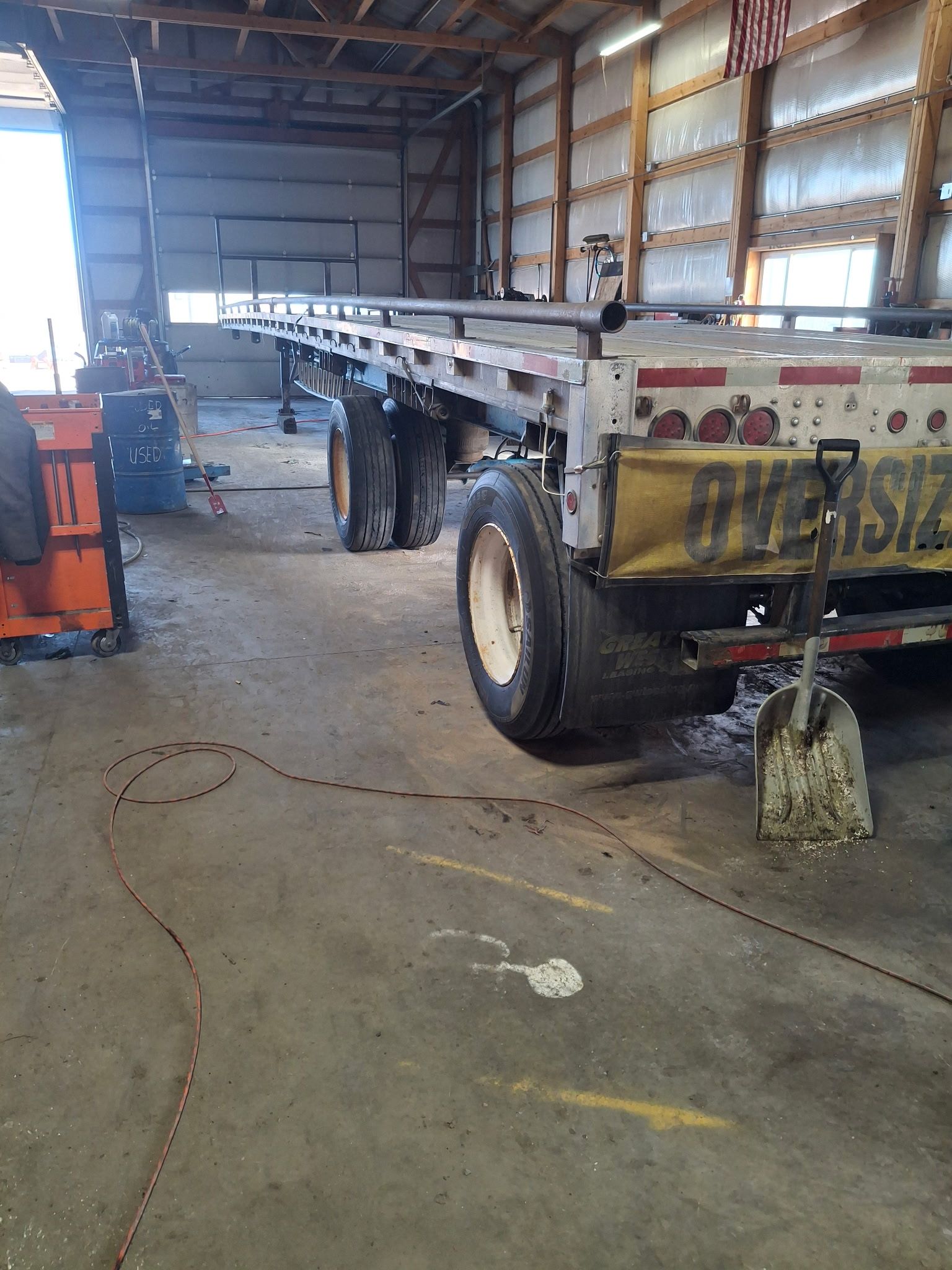 A person in workwear inspects a truck tire, taking notes on a clipboard, outdoors.