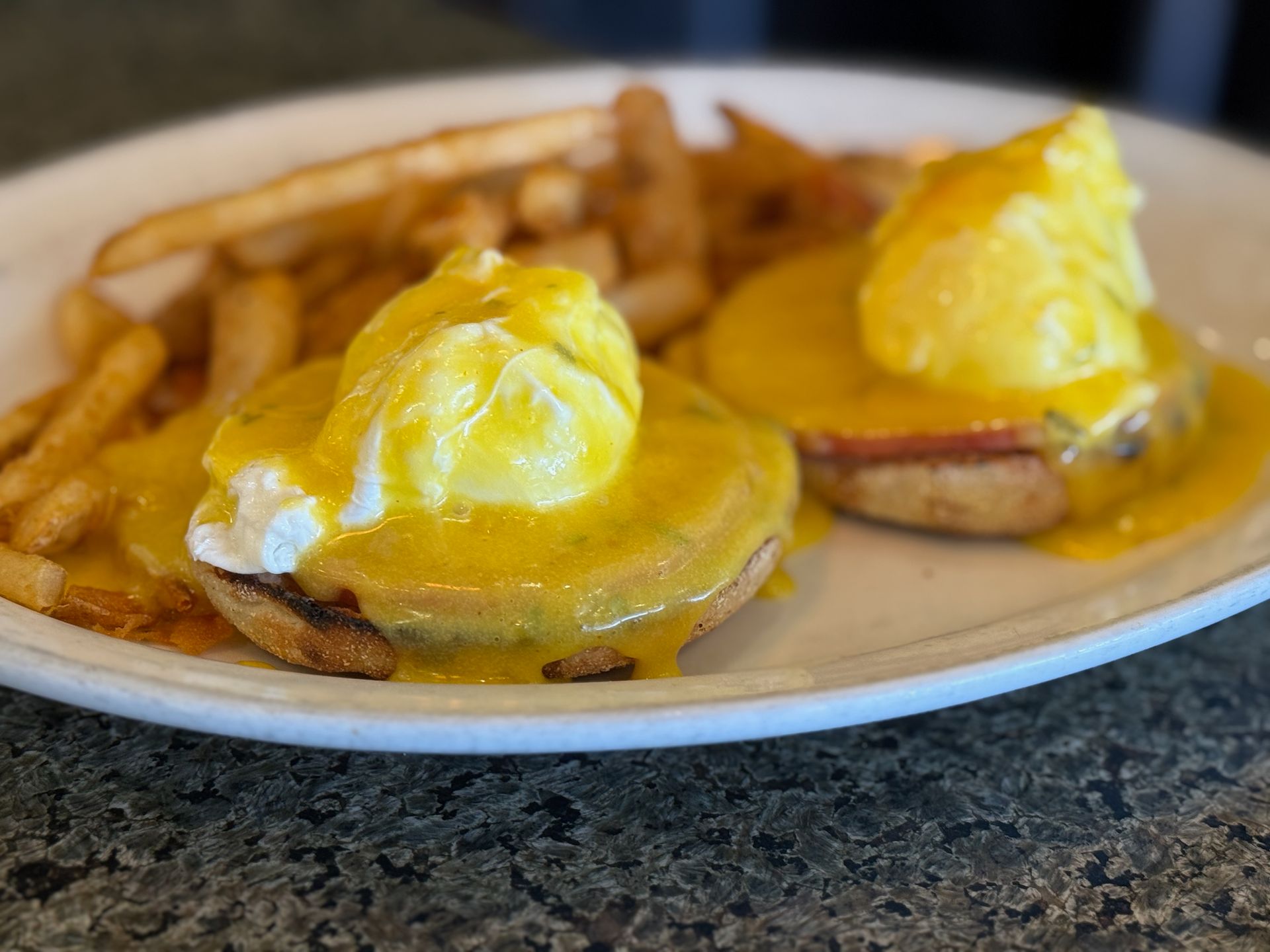 A plate of food with eggs benedict and french fries on a table.