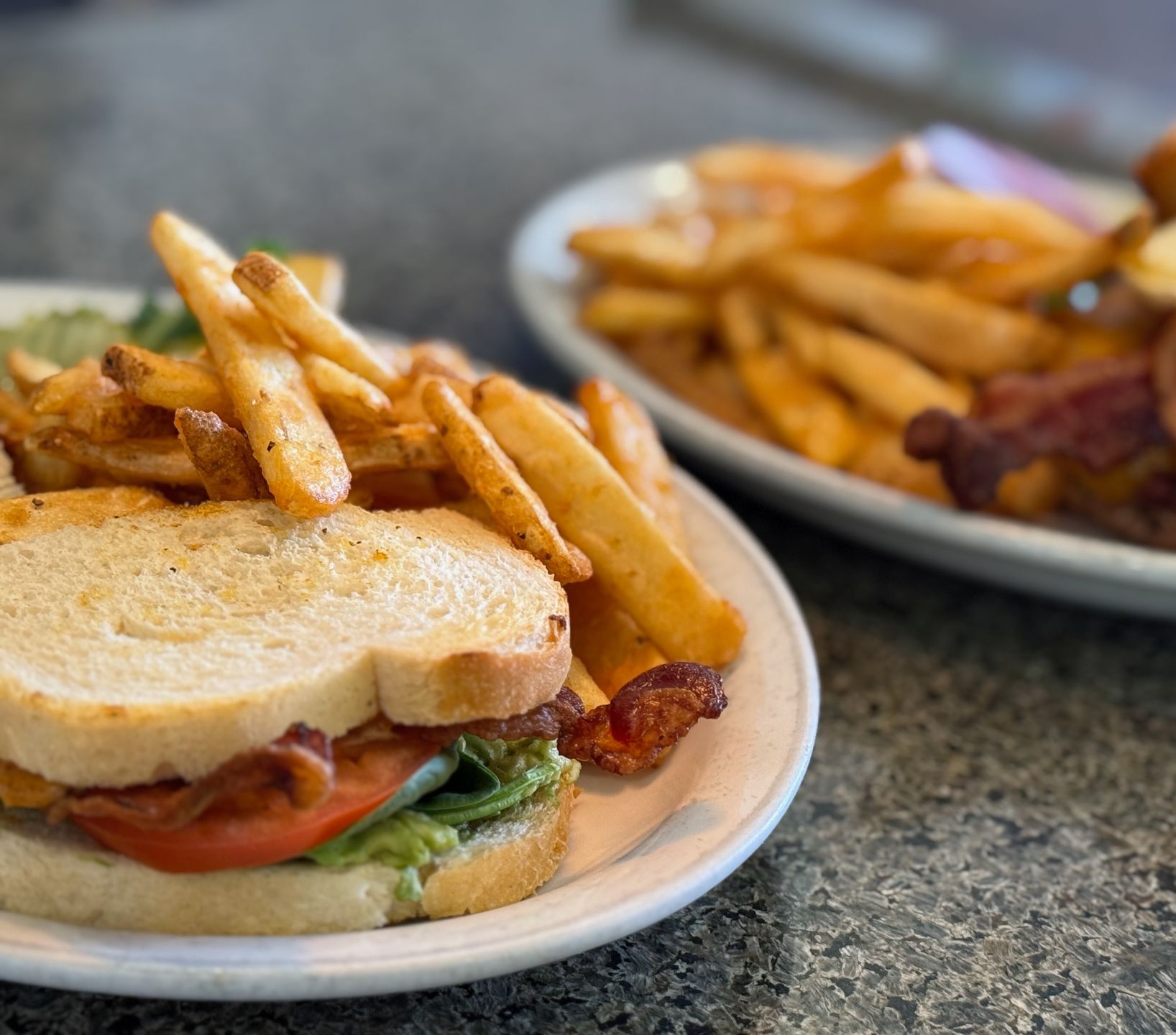 Two plates of food including a sandwich and french fries on a table.