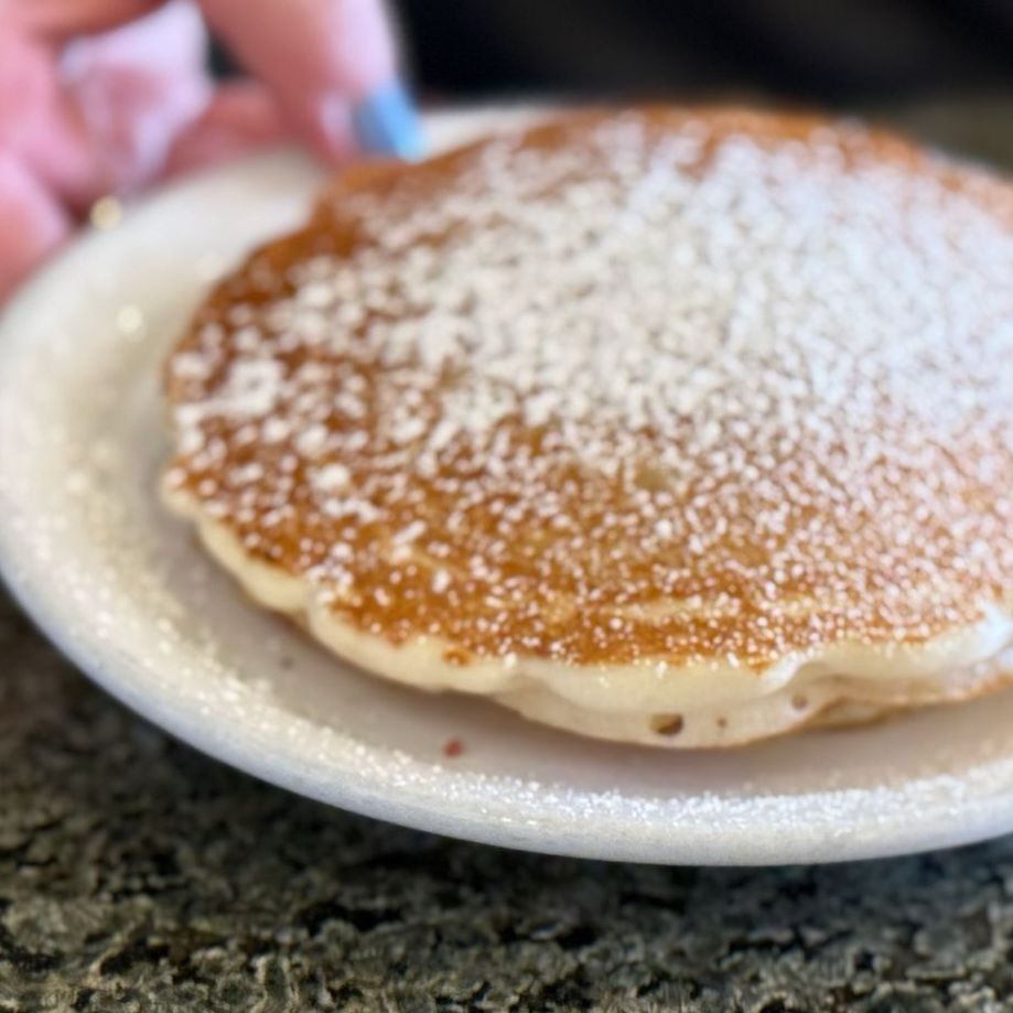Two pancakes on a white plate with powdered sugar on top.