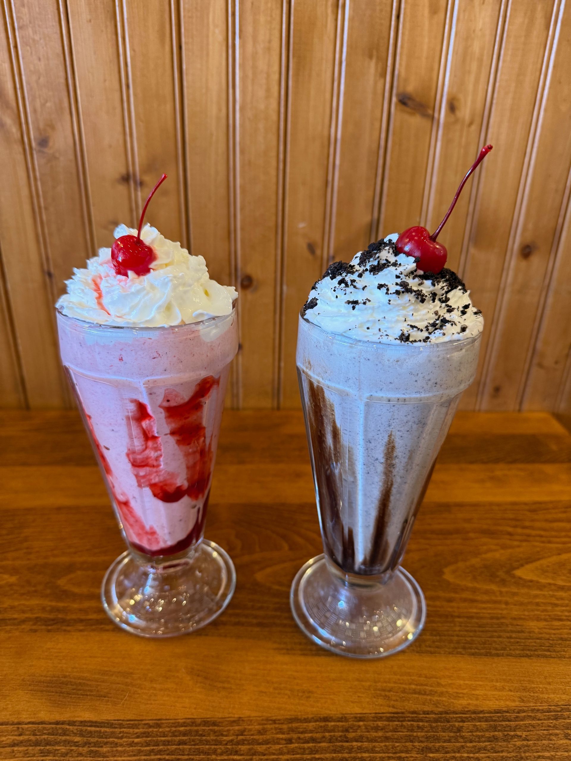 A strawberry smoothie in a glass with strawberries on a table.