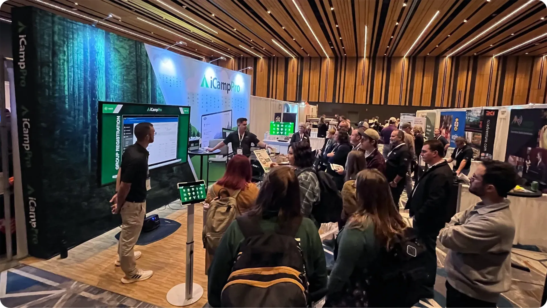 People watching a presentation at a conference. The presenter stands near a screen with the company logo.