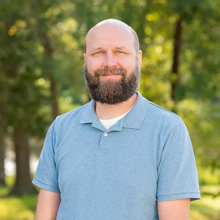 Man with a beard, wearing a blue polo shirt, smiling, standing outdoors.