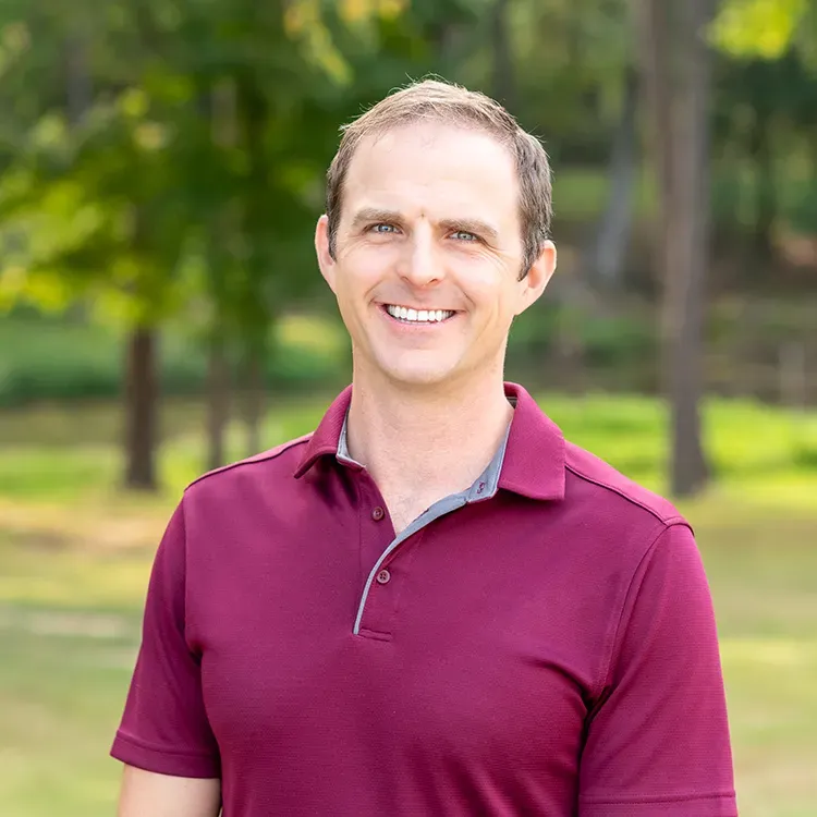 A smiling person wearing a maroon polo shirt