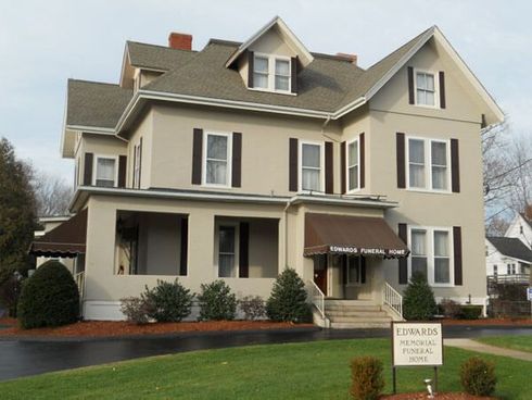 Large beige house with gray roof and white trim, viewed from the front on a cloudy day