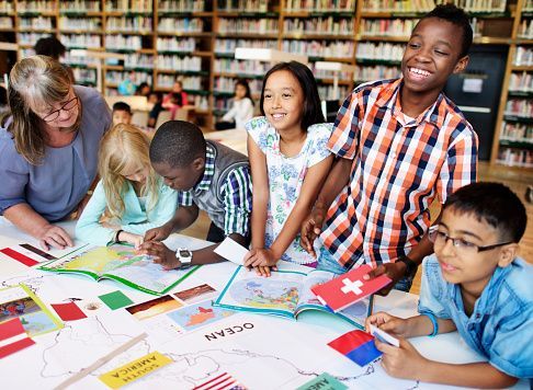 A group of children are sitting around a table in a library looking at a map.