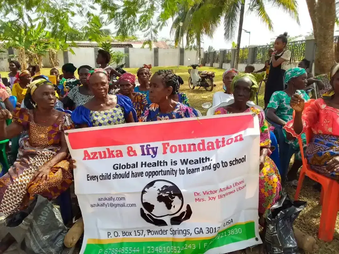 A group of people are sitting in chairs holding a sign that says azuka & ify foundation.