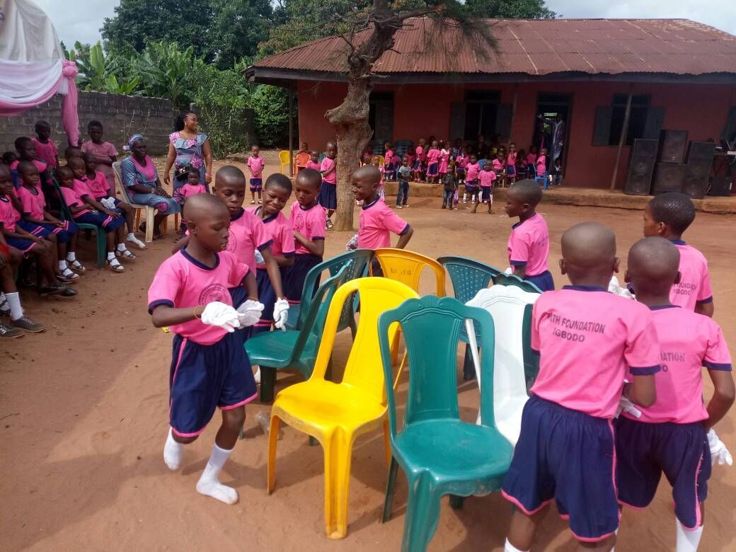 A group of children in pink shirts are standing around chairs