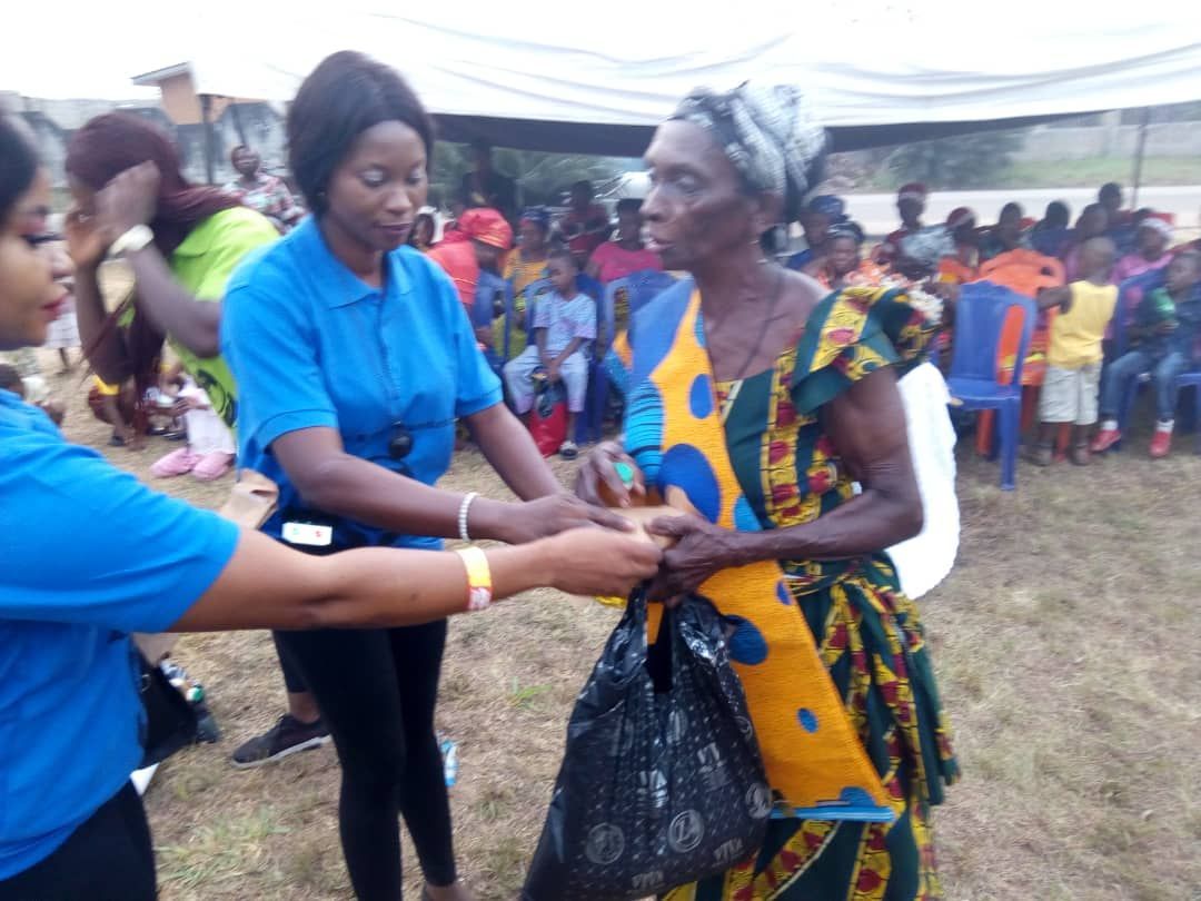 A woman in a blue shirt is giving an older woman a bag of food.