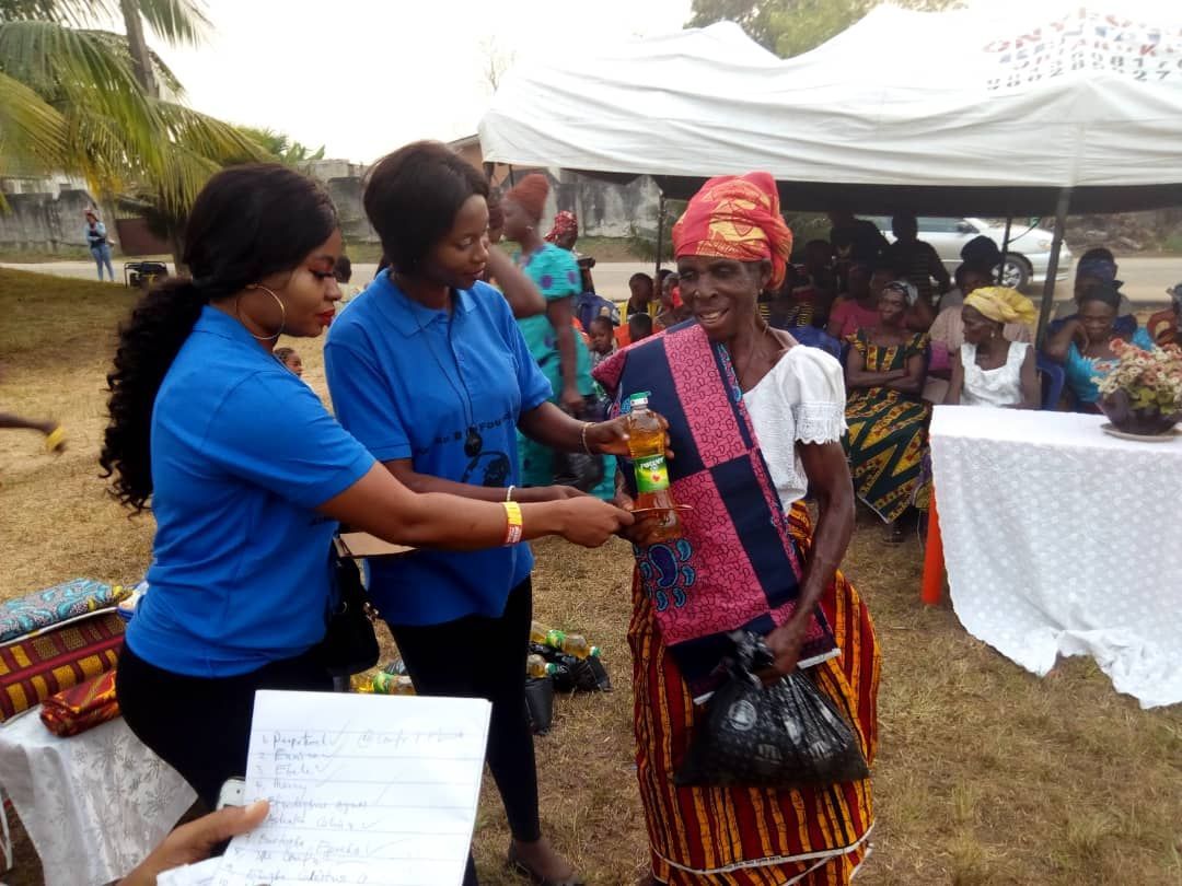 A woman in a blue shirt is giving a bottle of soda to another woman.