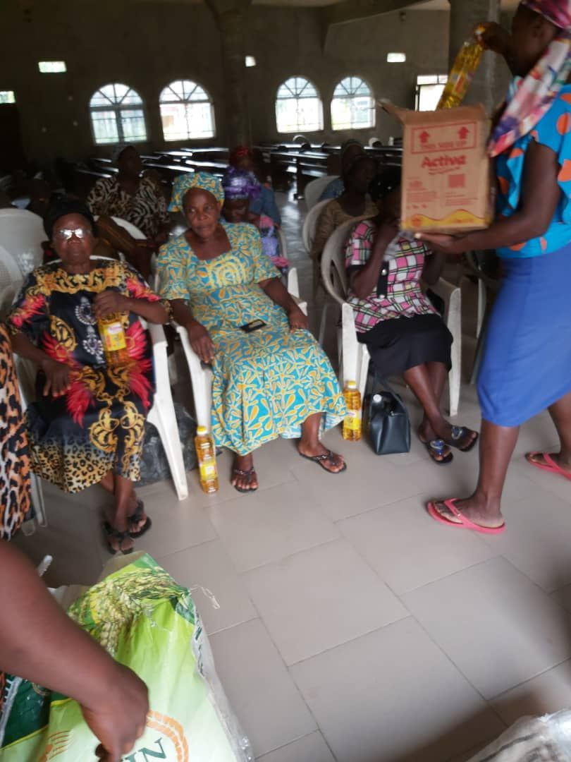 A woman is holding a box in front of a group of people sitting in chairs.