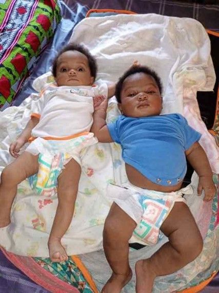 Two babies in diapers are laying next to each other on a bed.