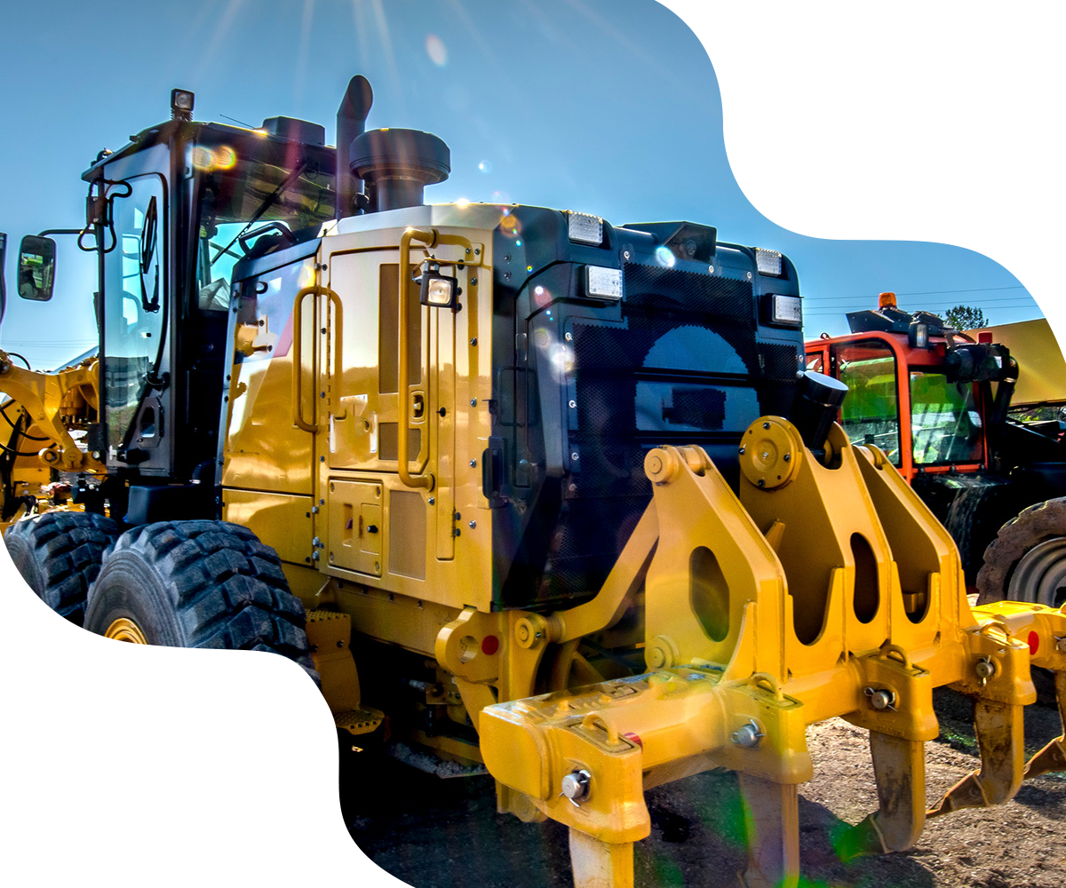 Yellow construction grader with attachments, outdoors in daylight.