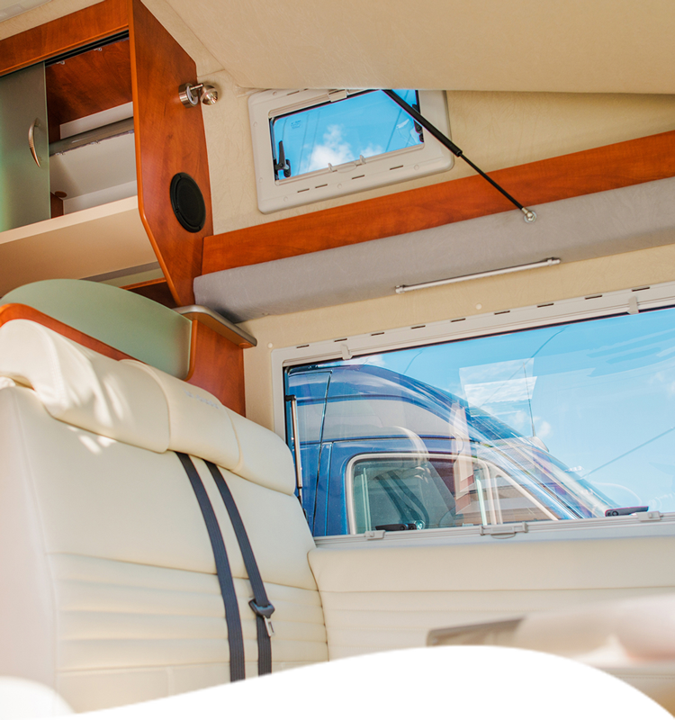 Interior of a white van with cream seating, wood trim, and a small window.