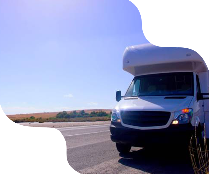 White RV on a road, under a bright blue sky. Dry landscape in the background.