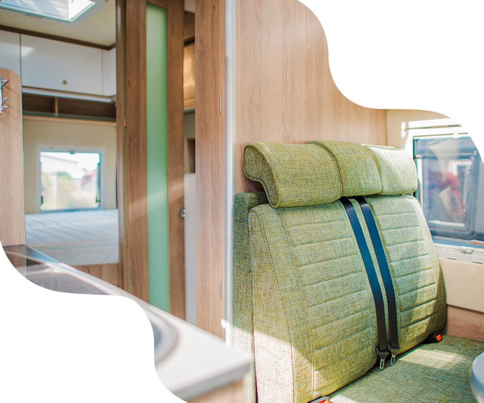 Interior of a campervan with green seating and light wood paneling. Sunlight streams through a window.