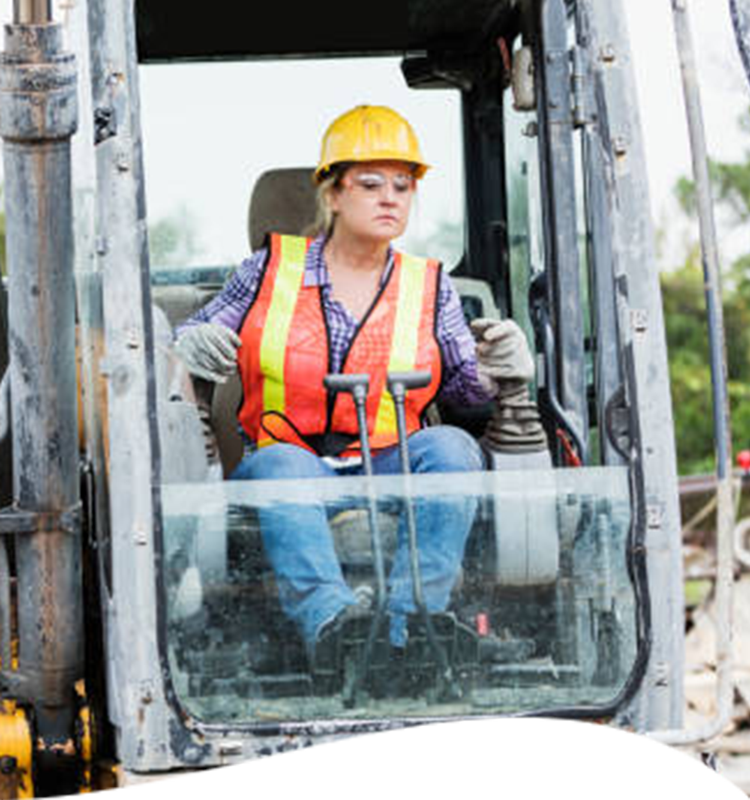 Woman operating construction equipment, wearing safety gear.