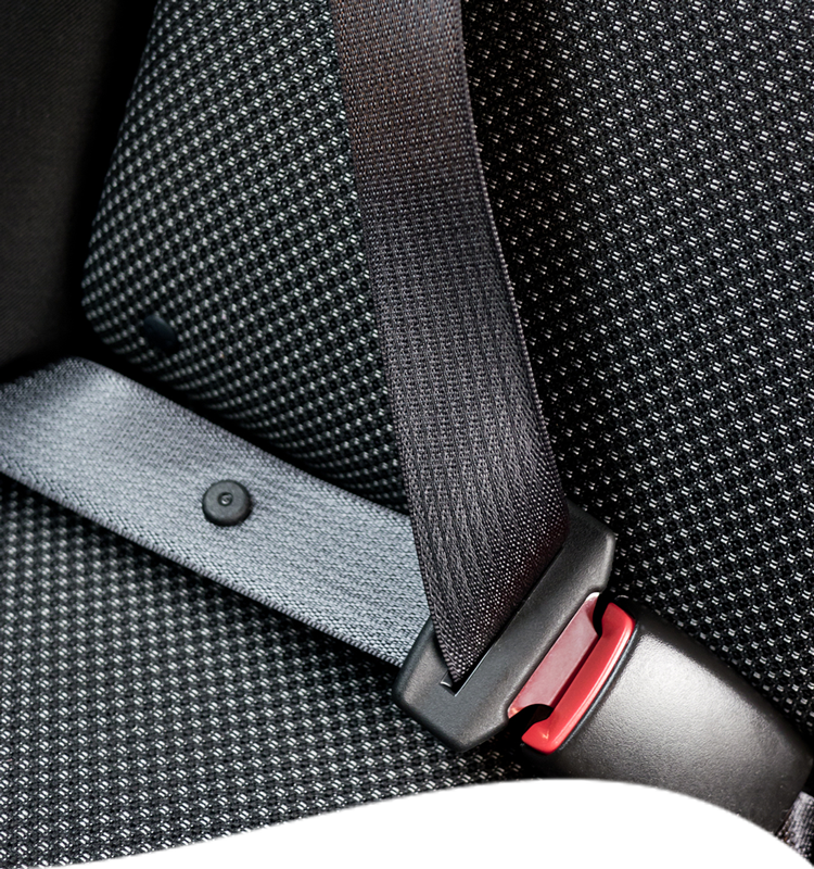 Black seat belt fastened, red release button, against patterned car seat.