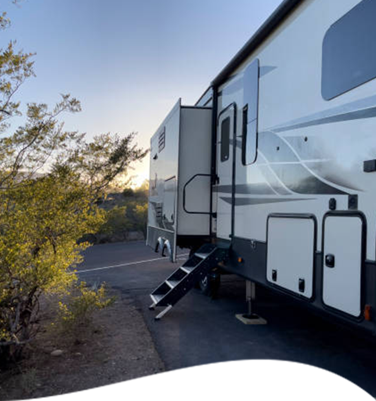 RV parked outdoors with steps extended. White exterior, slide-out open, in a desert-like setting.