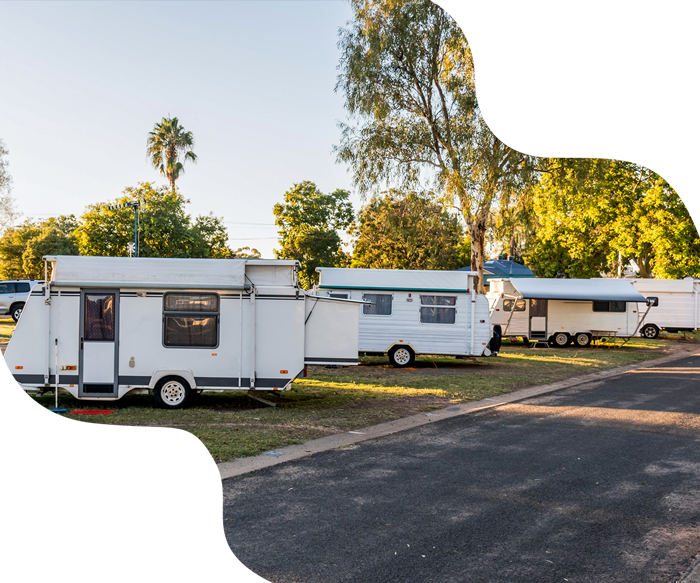 White campers parked on a paved lot, near trees, on a sunny day.