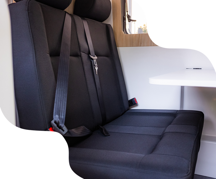 Black van bench seat with seat belts next to a white table.