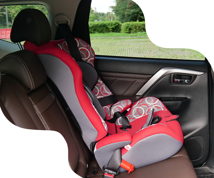 Red and gray child's car seat installed in the back seat of a brown car.