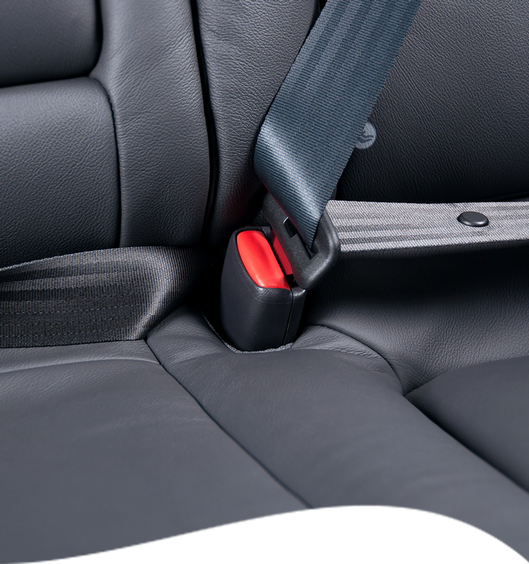 Close-up of black car seat with gray seatbelt fastened at the buckle, red release button visible.