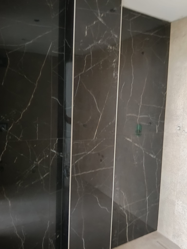 Porte dell'ascensore in marmo nero con una sottile giunzione, accanto a una parete in pietra chiara.