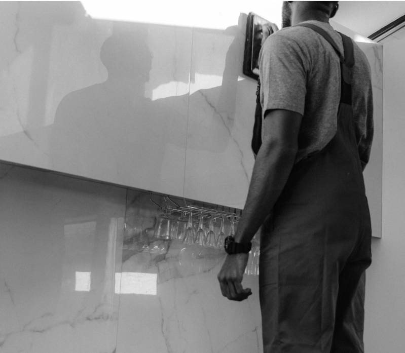 Persona con tuta scura in piedi accanto a un lavandino a muro in una stanza interna piastrellata.