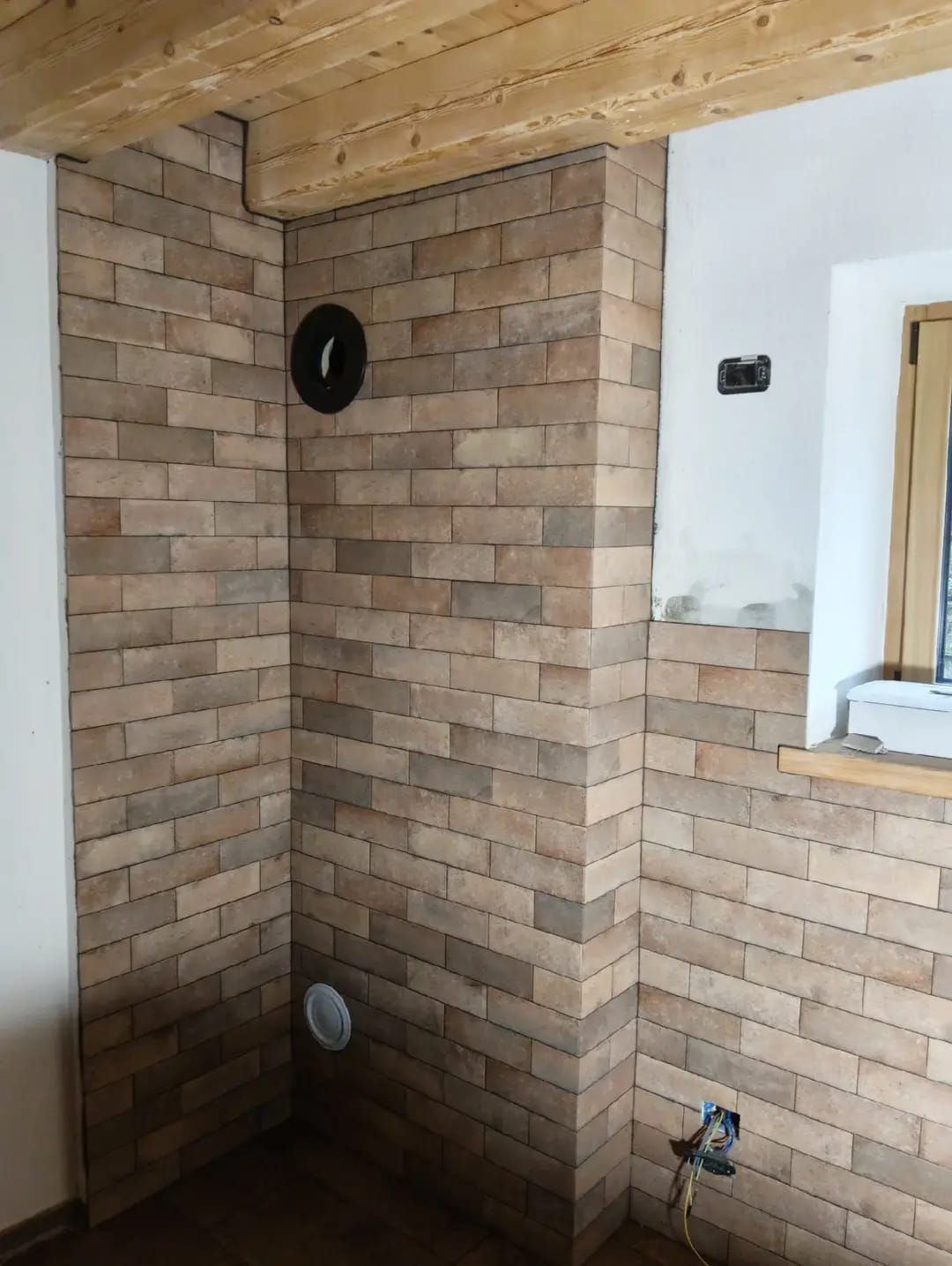 Parete del bagno parzialmente piastrellata con aperture per gli impianti idraulici e un'apertura per la finestra.