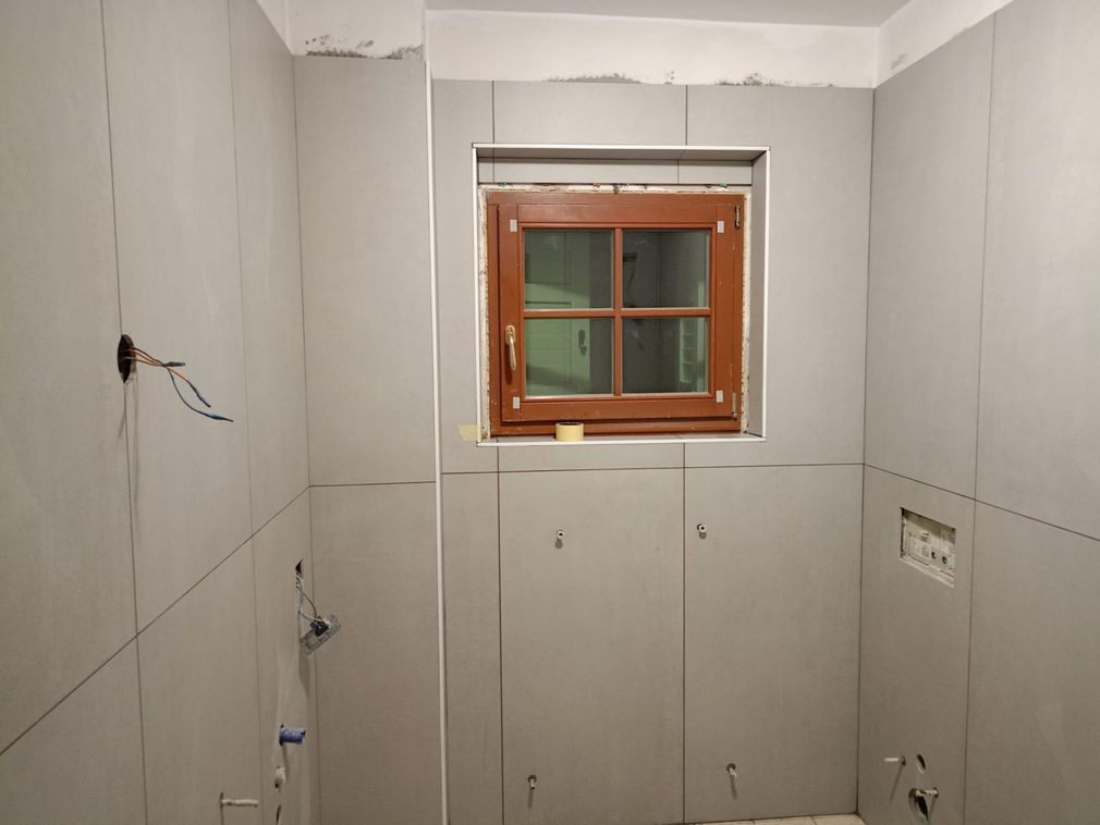Bagno parzialmente piastrellato in fase di ristrutturazione con una piccola finestra sulla parete di fondo.