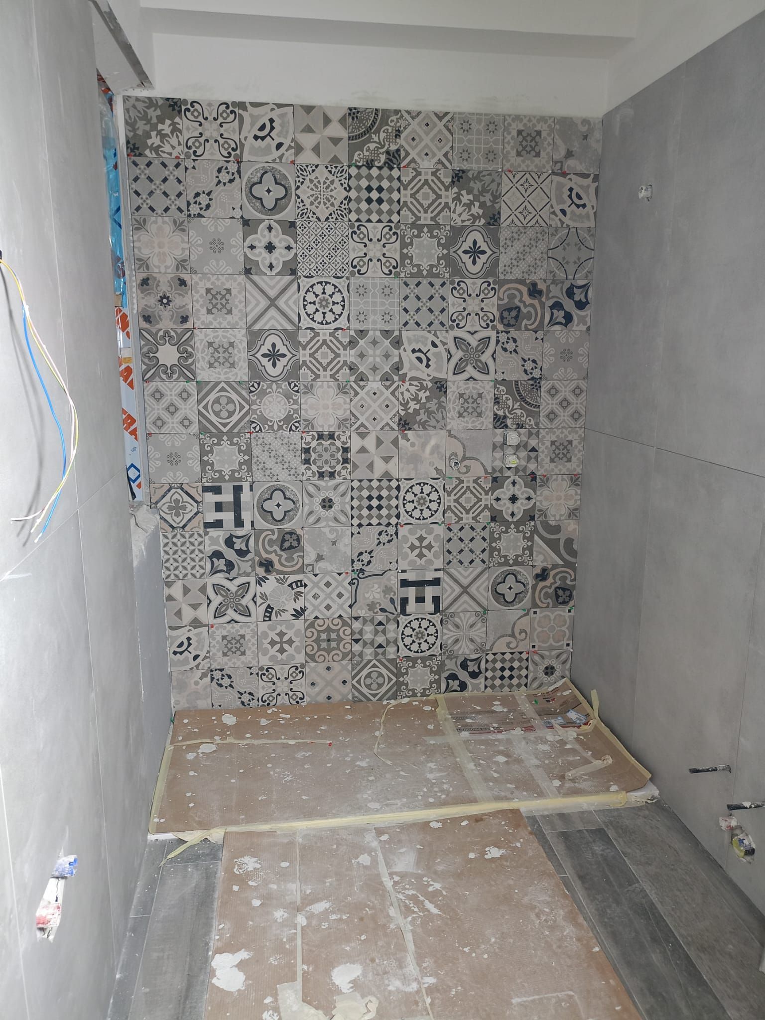 Piccolo bagno non rifinito con parete decorativa piastrellata e pavimento in cemento grezzo in fase di costruzione