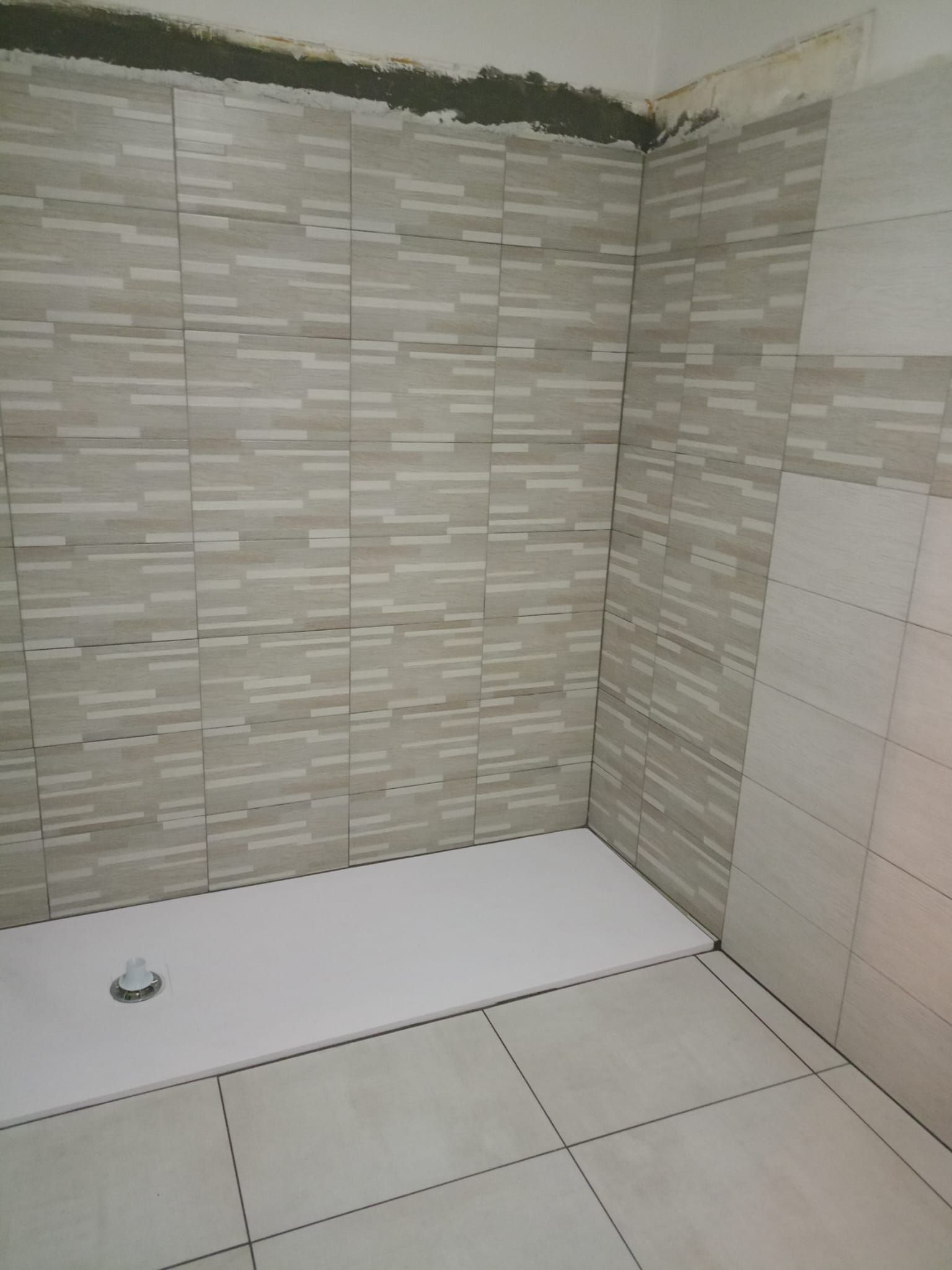 Piccolo angolo del bagno piastrellato con piatto doccia bianco e piastrelle a parete beige.
