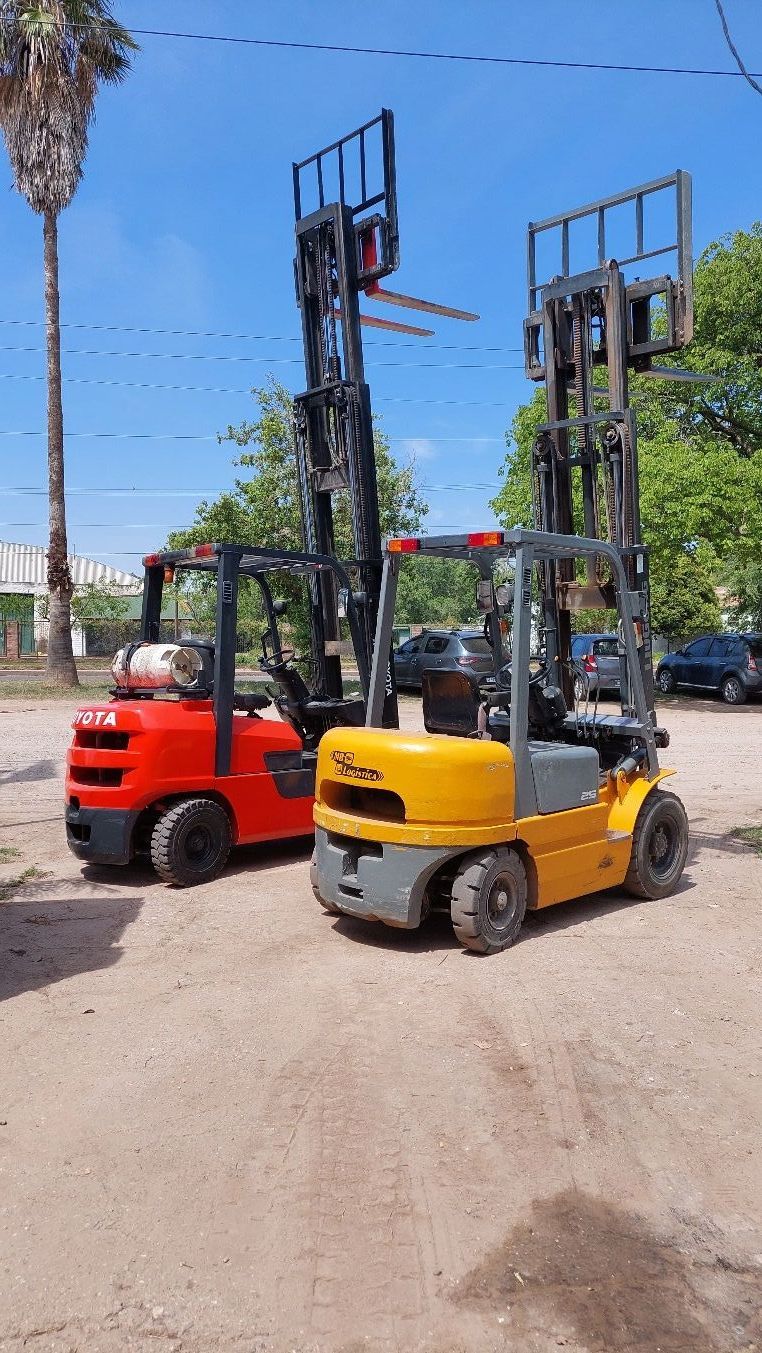 Dos carretillas elevadoras están estacionadas una al lado de la otra en un lote de tierra.