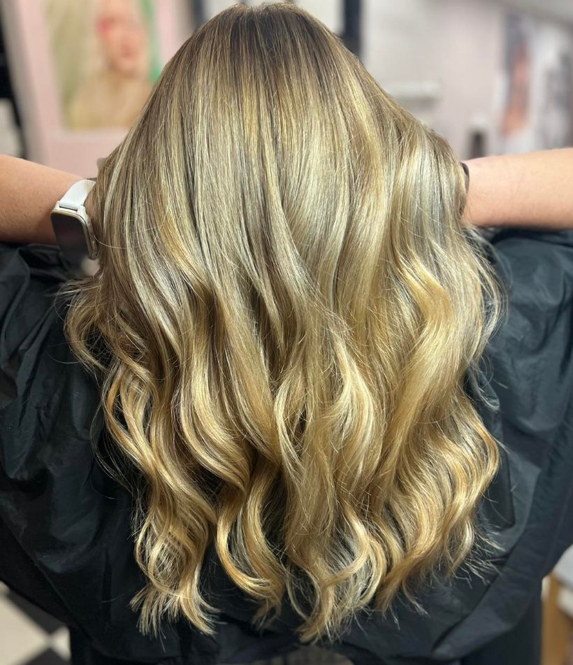 A Woman with Long Blonde Hair Is Sitting in A Chair with Her Hands Behind Her Head — Ammo Hair and Beauty In Maclean, NSW