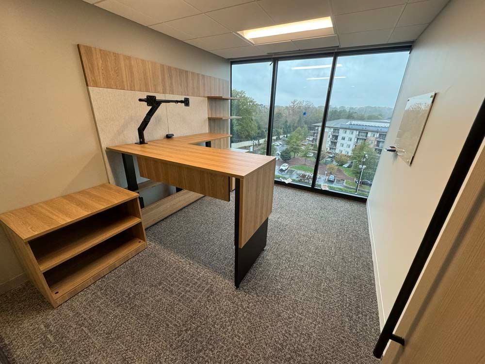 A small office with a desk , shelves , and a large window.