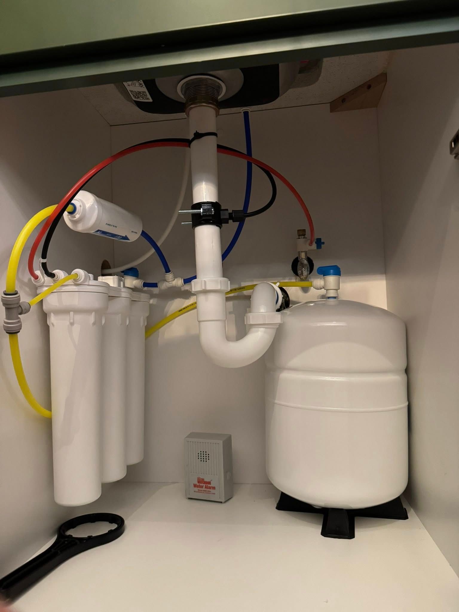 Under-sink water filtration system with white tanks, filter canisters, and colored tubing