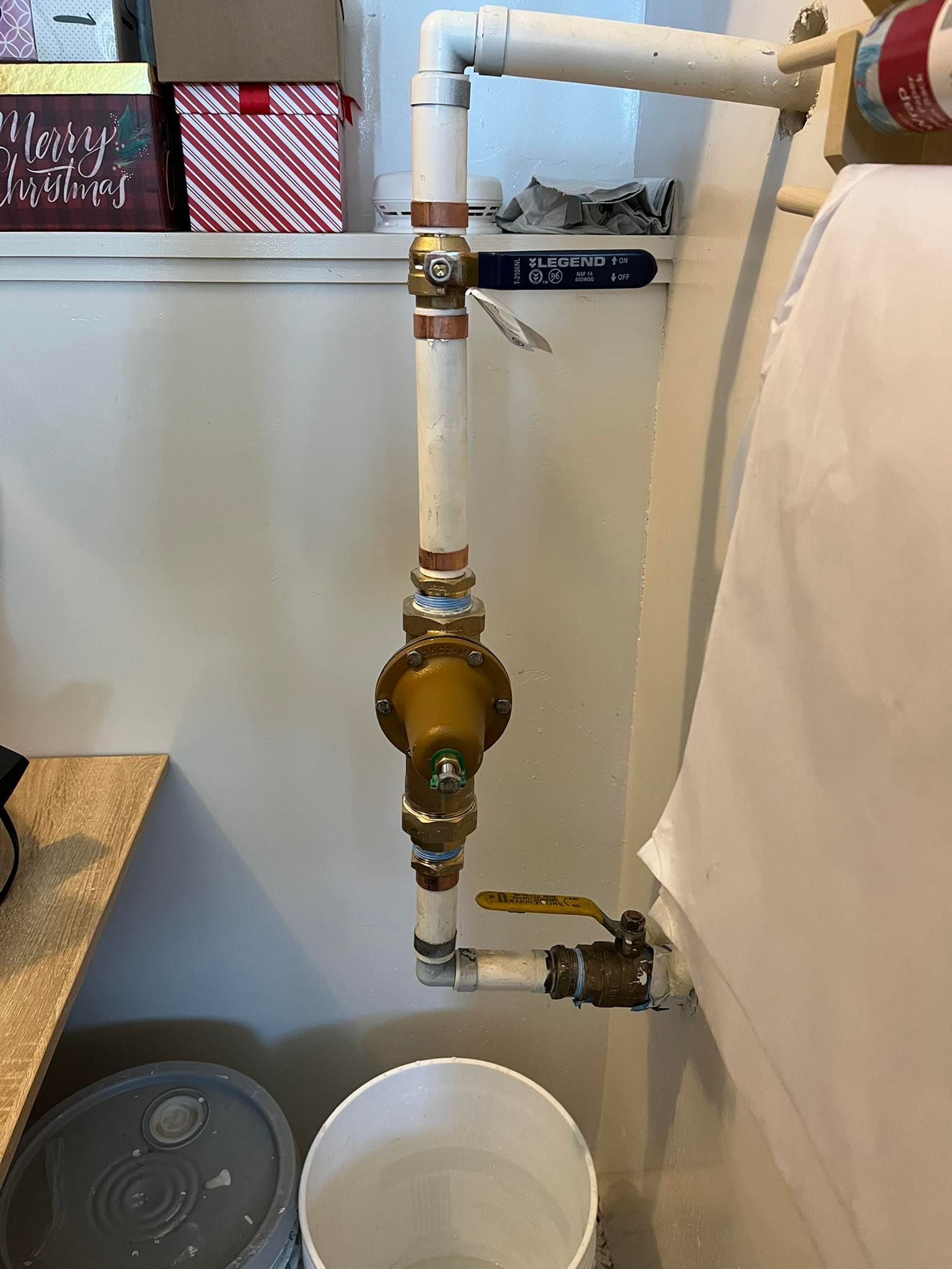 Vertical plumbing pipes with a brass valve next to a white bucket in a utility room