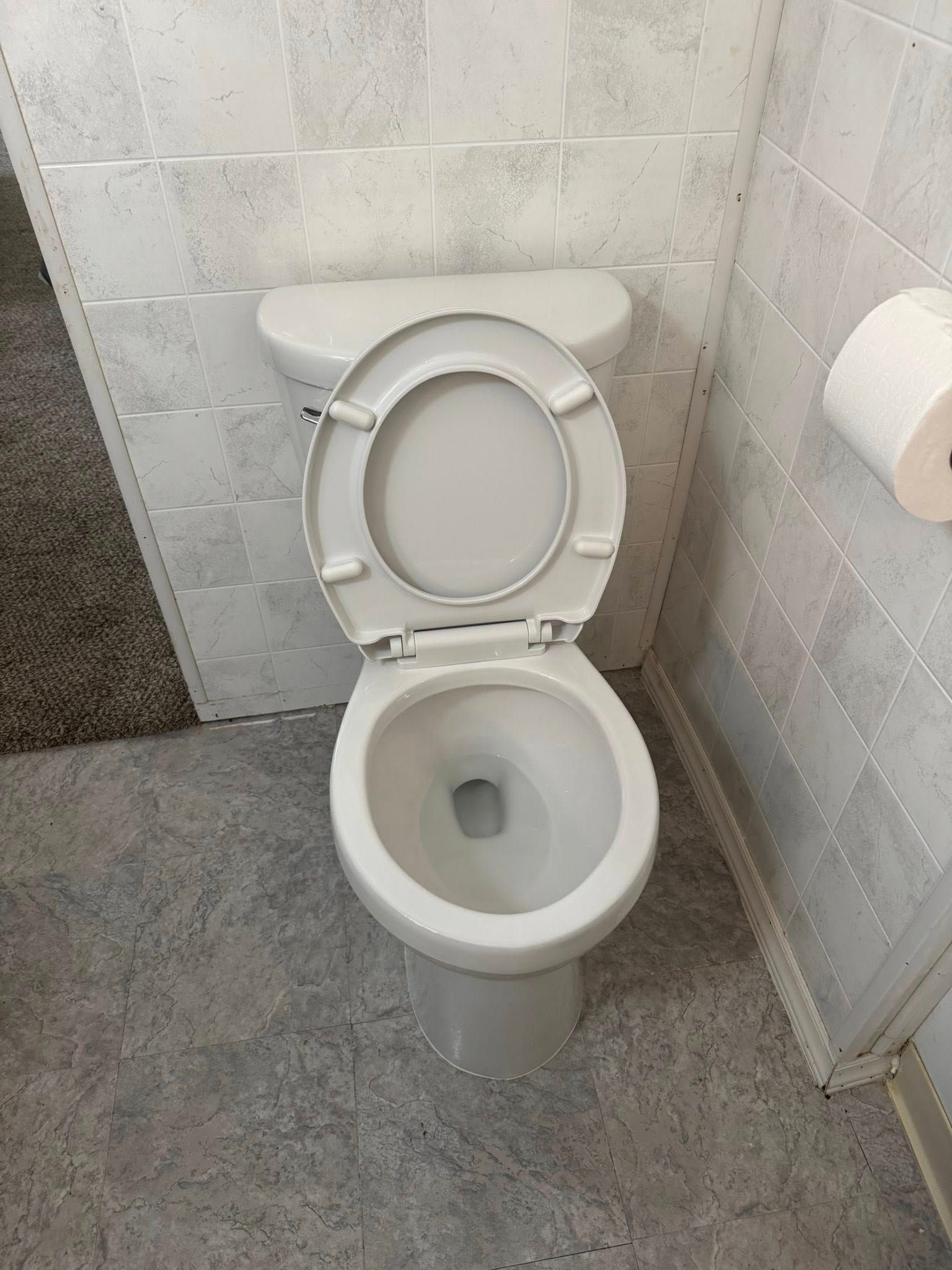 Open toilet in a tiled restroom with a toilet paper roll on the right wall.