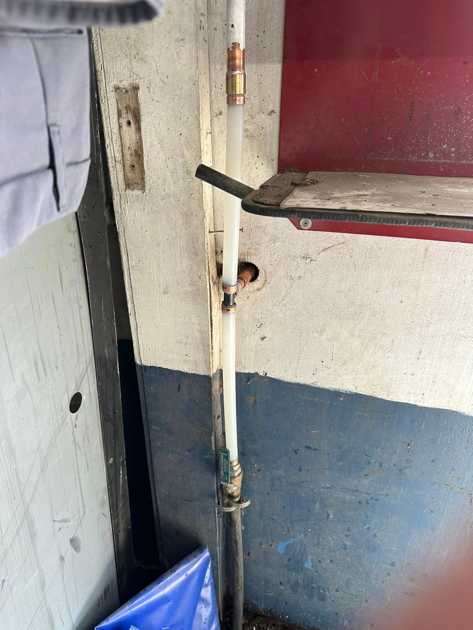 Narrow indoor corner with a metal lever, worn wall, and blue trash bag at the bottom