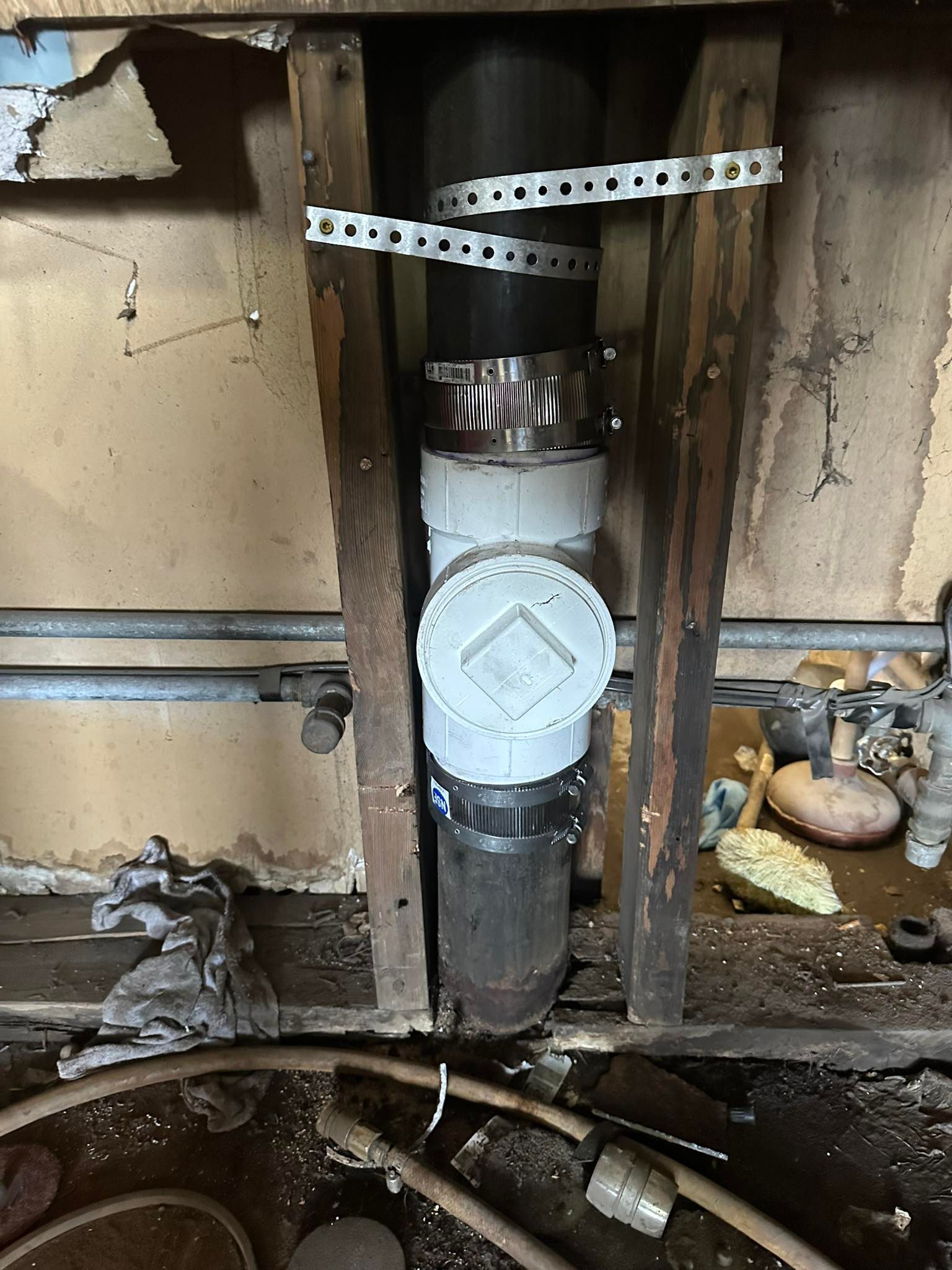 Vertical metal pipe in a wall opening, wrapped with white insulation and secured by perforated straps.