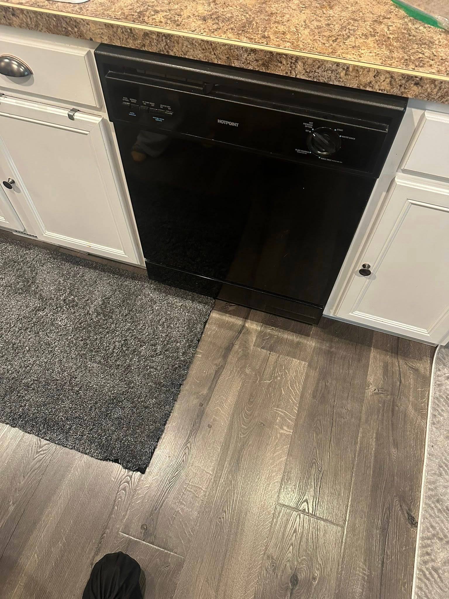 Black dishwasher under a speckled countertop between white cabinets in a kitchen