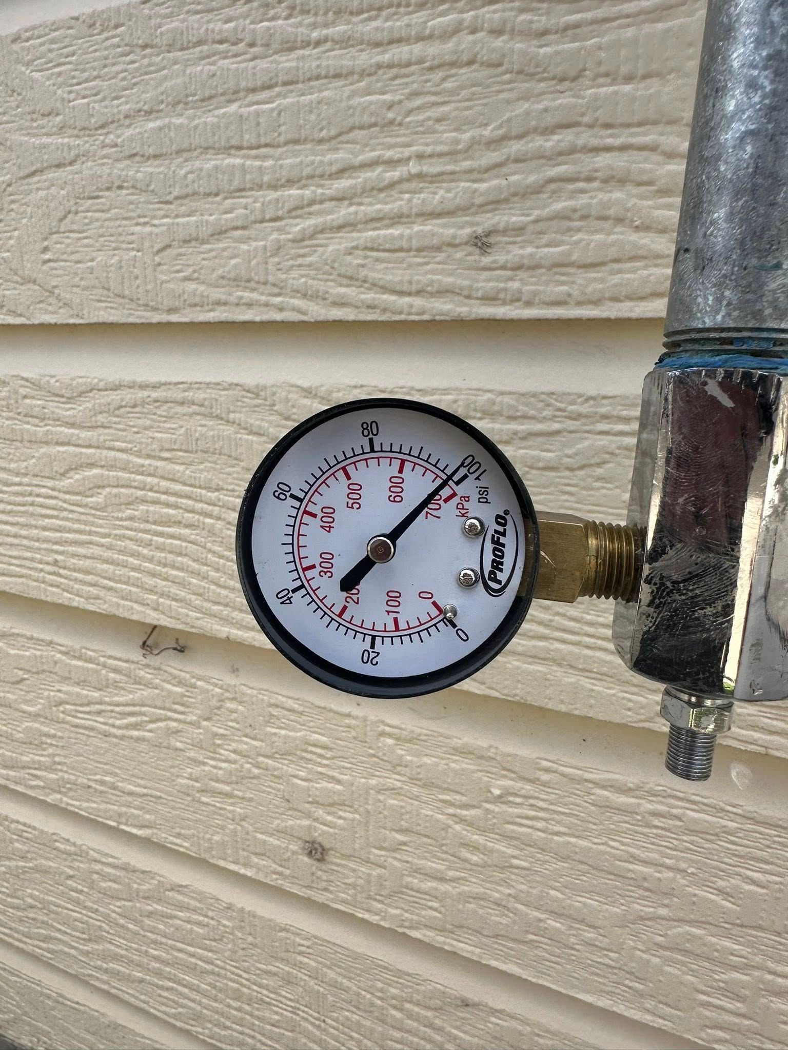 Pressure gauge mounted on beige siding, showing a low reading beside a metal pipe.