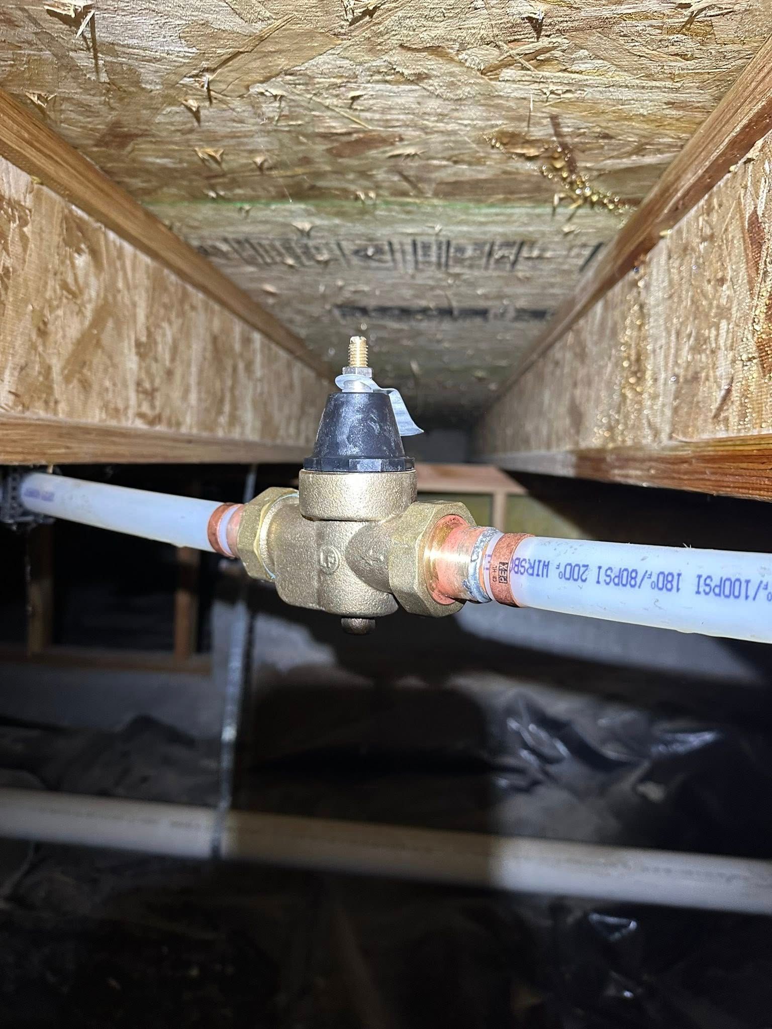 Pipe valve and blue PVC pipes inside a cramped, stained crawlspace ceiling opening