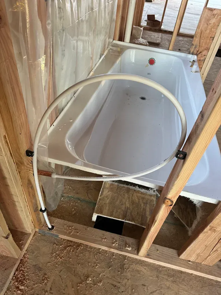 Freestanding bathtub under construction in a framed bathroom, with exposed plumbing and insulation.