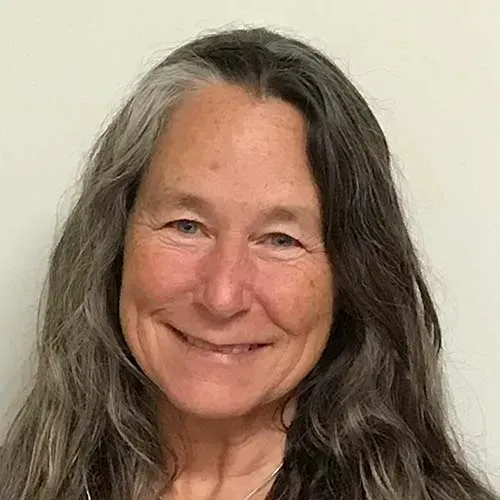 A woman with long gray hair is smiling for the camera.