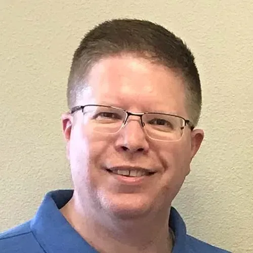 A man wearing glasses and a blue shirt is smiling for the camera.