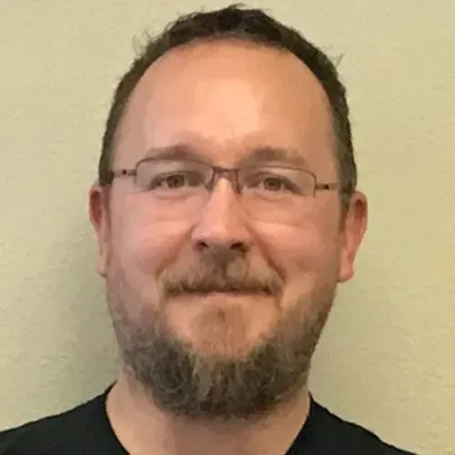 A man with a beard and glasses is smiling for the camera.